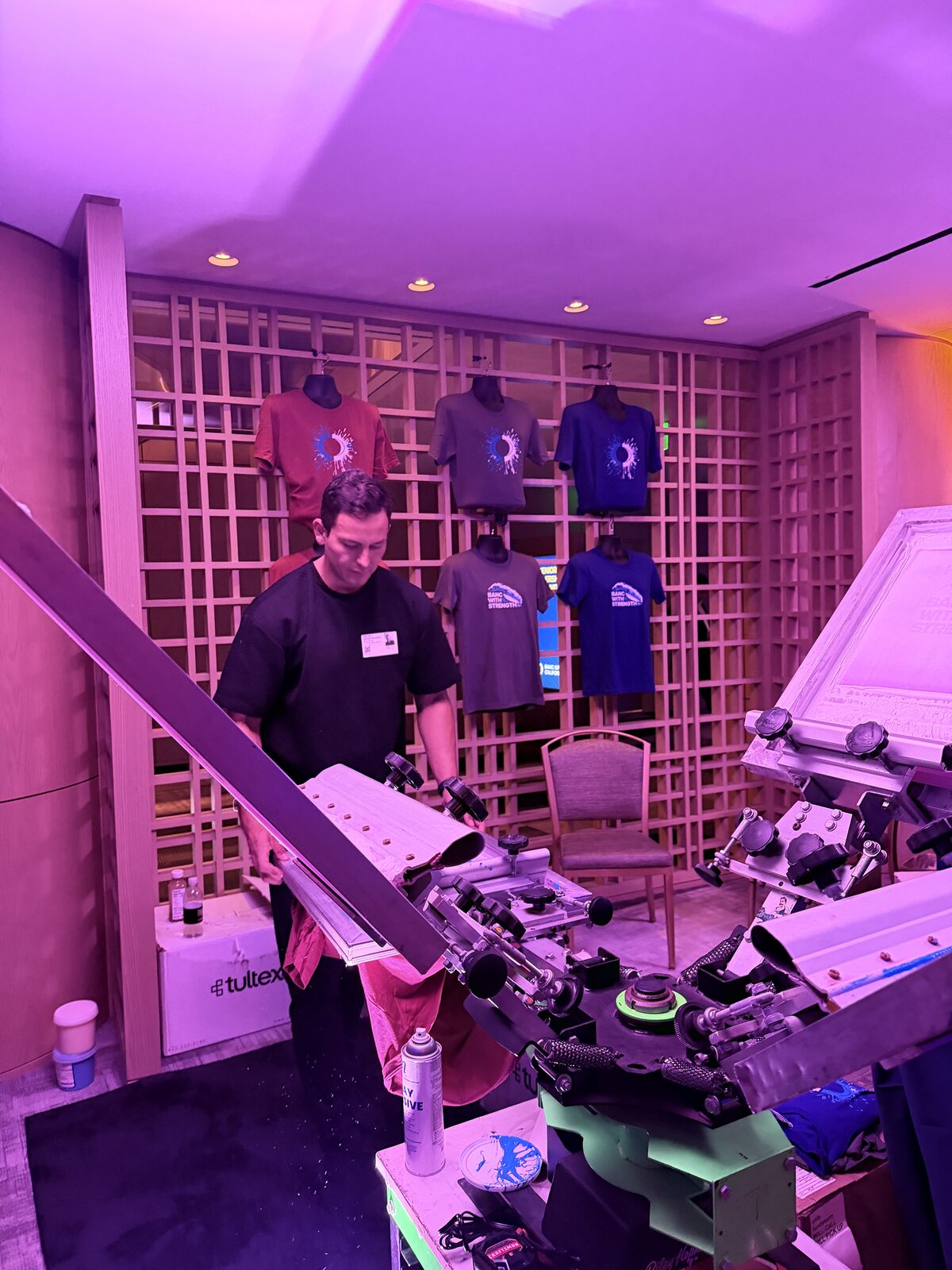 A crew member loading a shirt onto a screen printing press at a live event