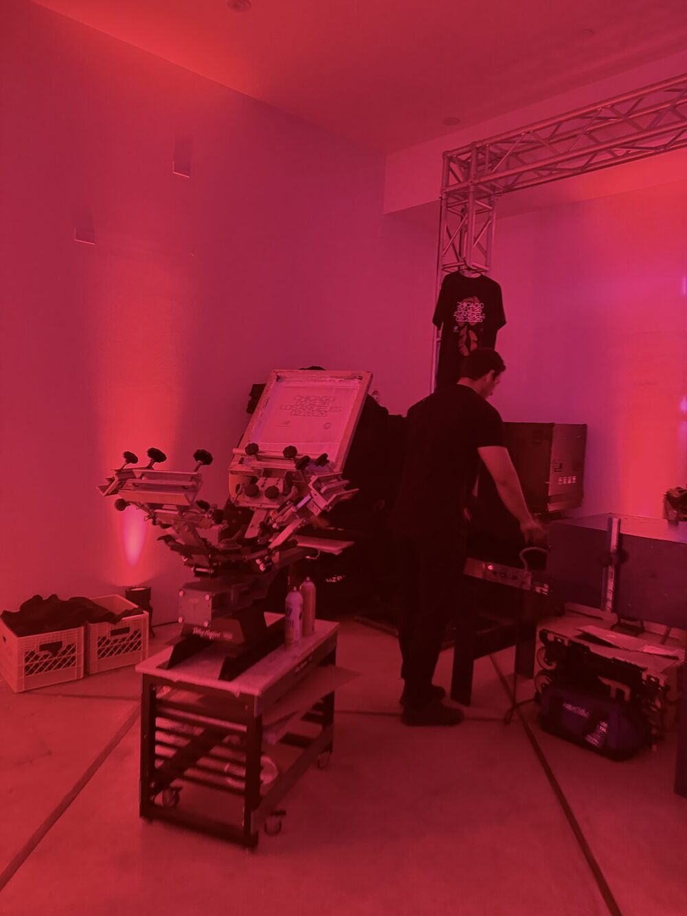A heat press rig on an event table with transfer sheets and tools laid out for production